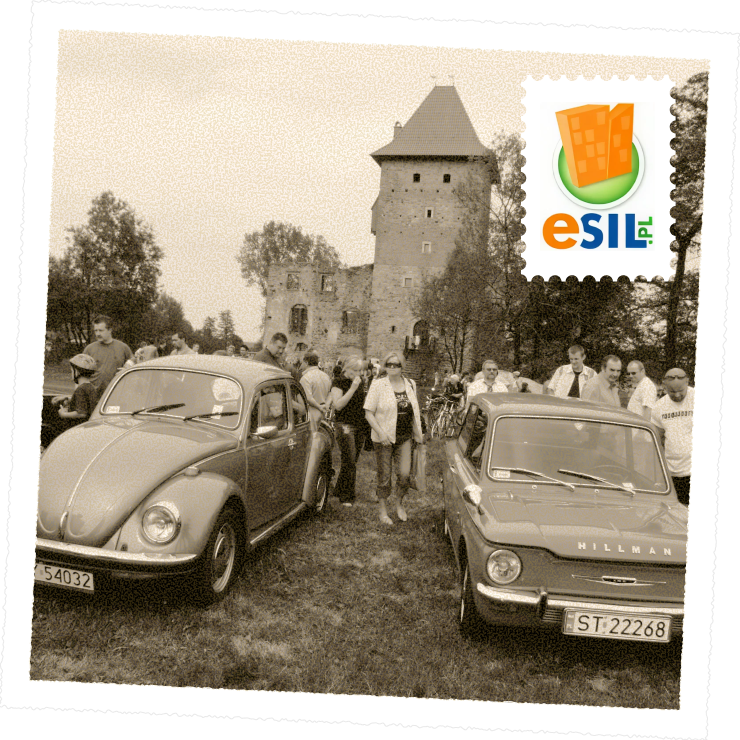 Czarno-białe zdjęcie plenerowego zlotu miłośników zabytkowych aut. Na pierwszym planie dwa klasyczne samochody – Volkswagen Garbus i Hillman, a w tle ruiny średniowiecznego zamku i zgromadzeni ludzie.