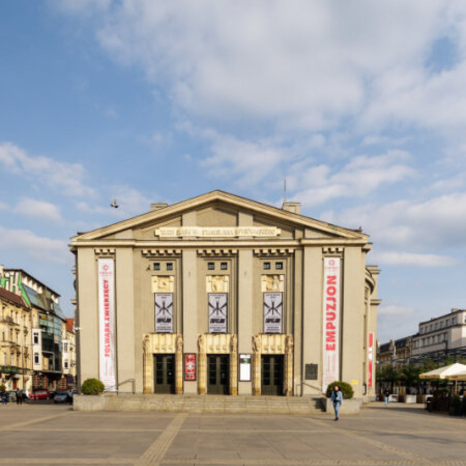 "Frontowa fasada Teatru Śląskiego z widocznym napisem 'TEATR ŚLĄSKI IM. STANISŁAWA WYSPIAŃSKIEGO'. Na budynku umieszczono pionowe banery oraz reklamy spektakli teatralnych."