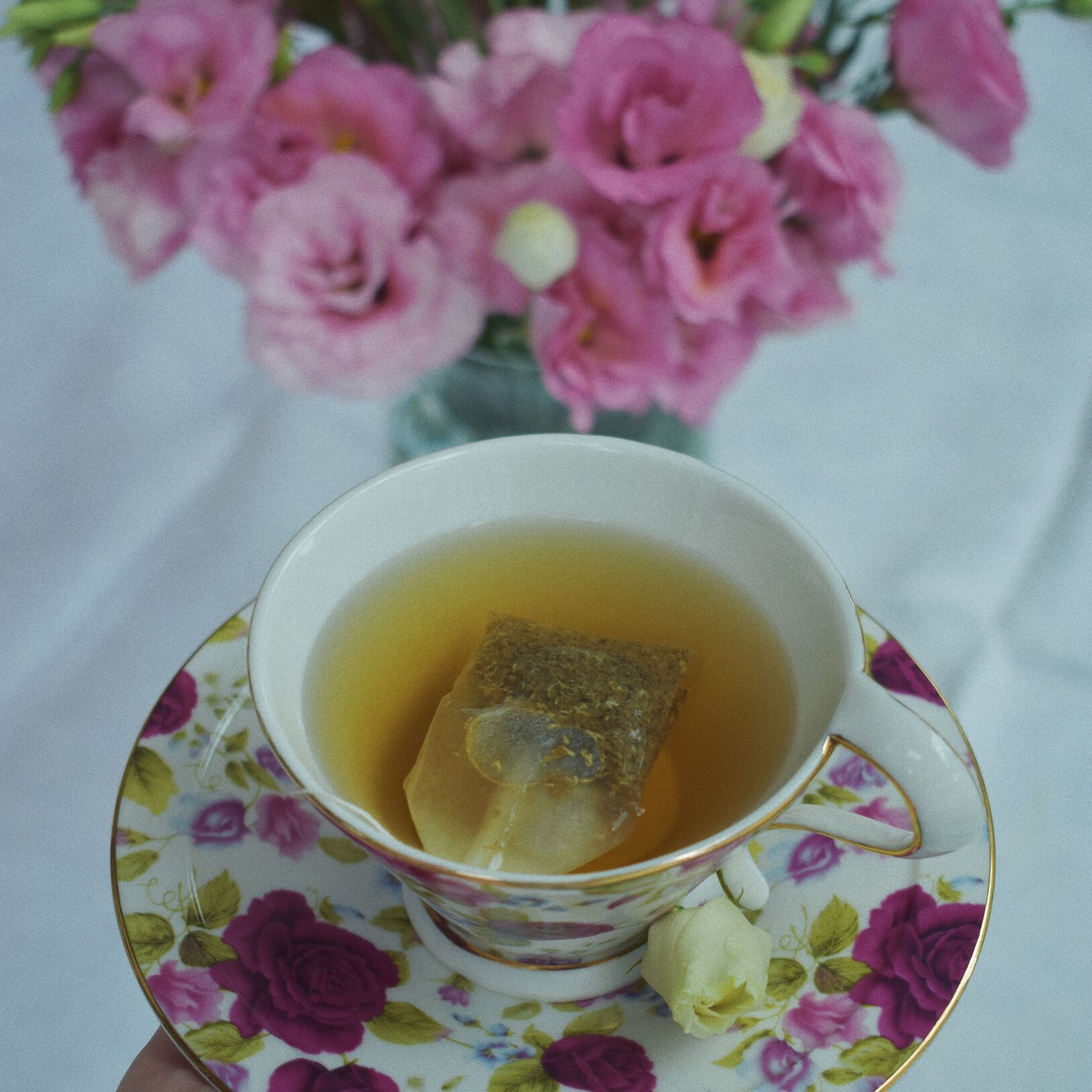 porcelanowa zdobiona filiżanka z herbatą, w tle różowe kwiaty