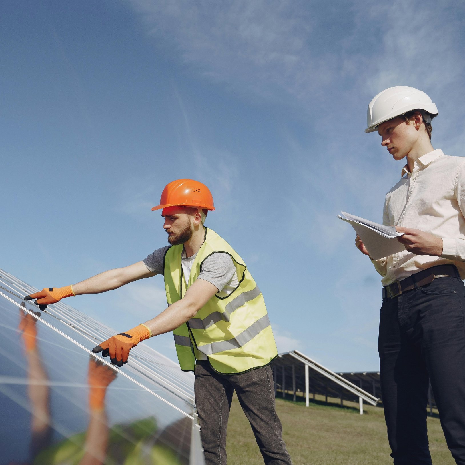 dwóch inżynierów w kamizelkach odblaskowych nad panelami fotowoltaicznymi