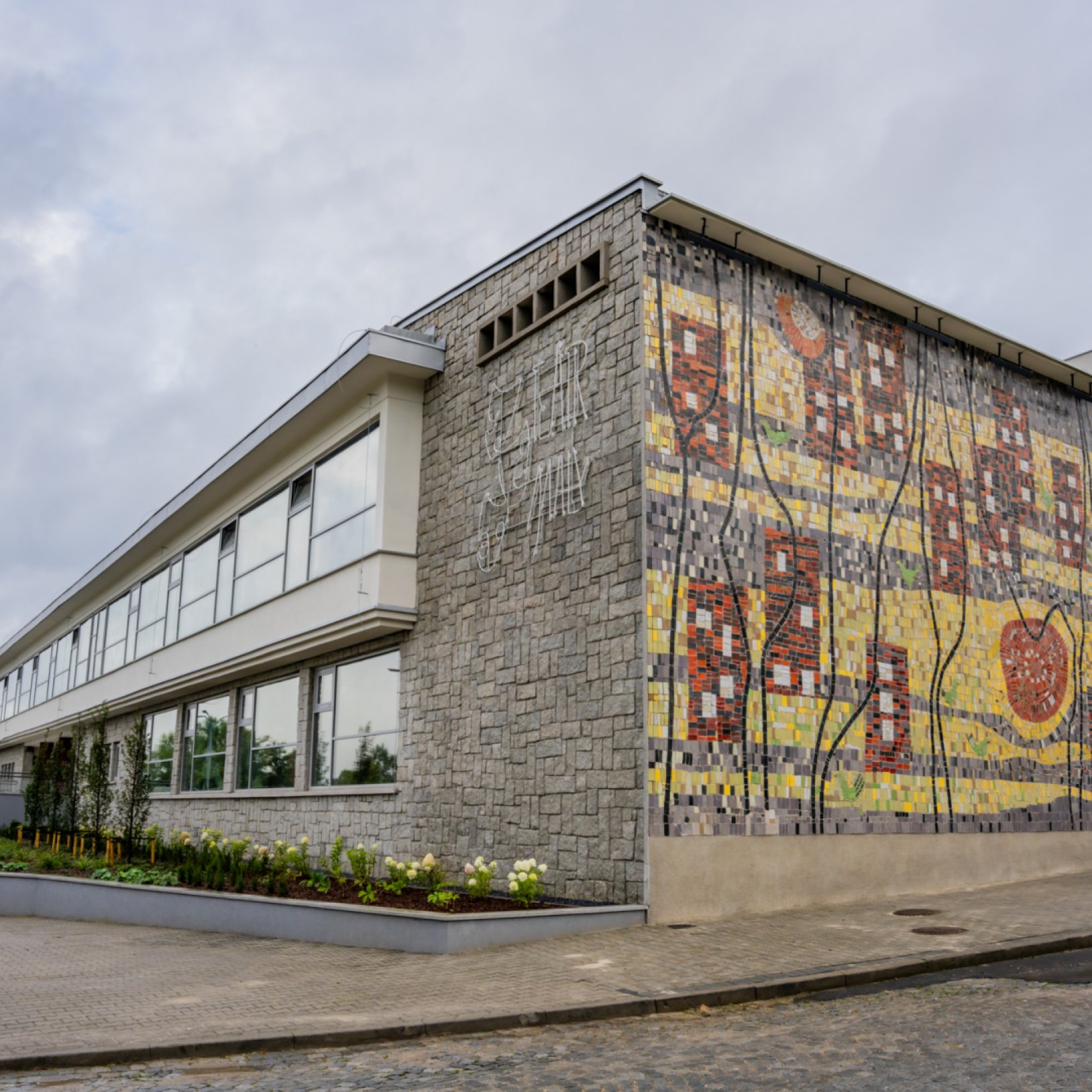 Zewnętrzny widok Teatru Małego w Tychach z charakterystyczną mozaiką na ścianie bocznej. Budynek ma elewację z kamienia i dużą ilość okien w nowoczesnym stylu.