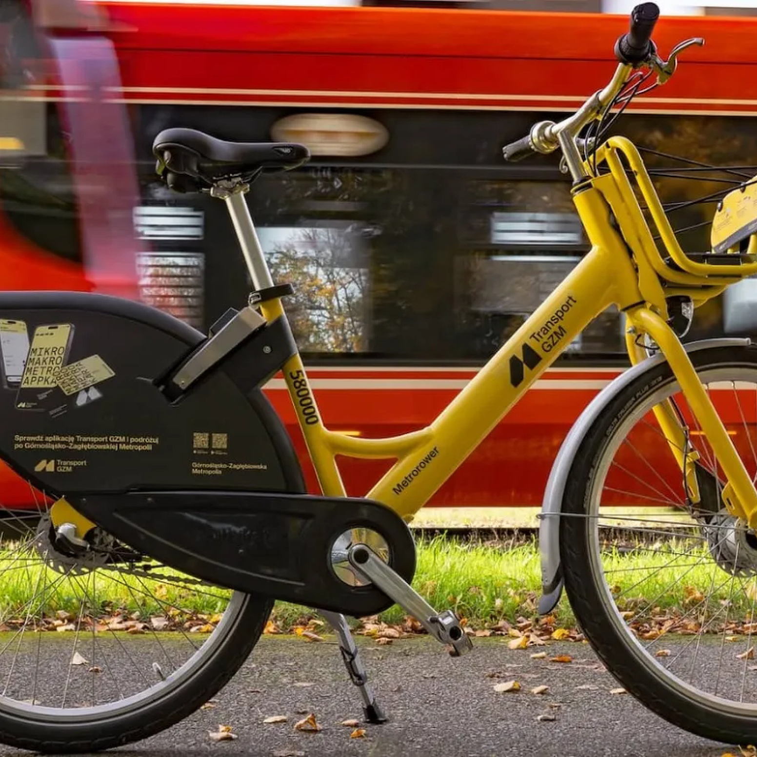 Żółty rower miejski na tle przejeżdżającego tramwaju