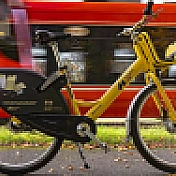 Żółty rower miejski na tle przejeżdżającego tramwaju