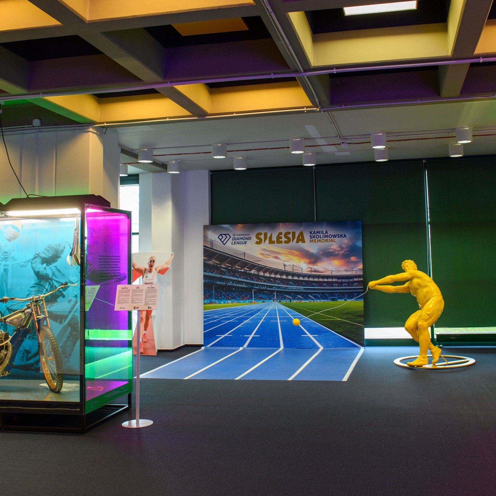 "Widok z góry na stadion z niebieską bieżnią lekkoatletyczną i zieloną murawą. Trybuny w kolorach niebieskim i żółtym tworzą zamknięty pierścień wokół boiska."