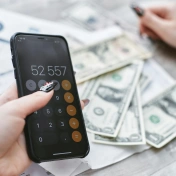 zdjęcie kalkulatora, pieniędzy i ręki trzymającej długopis