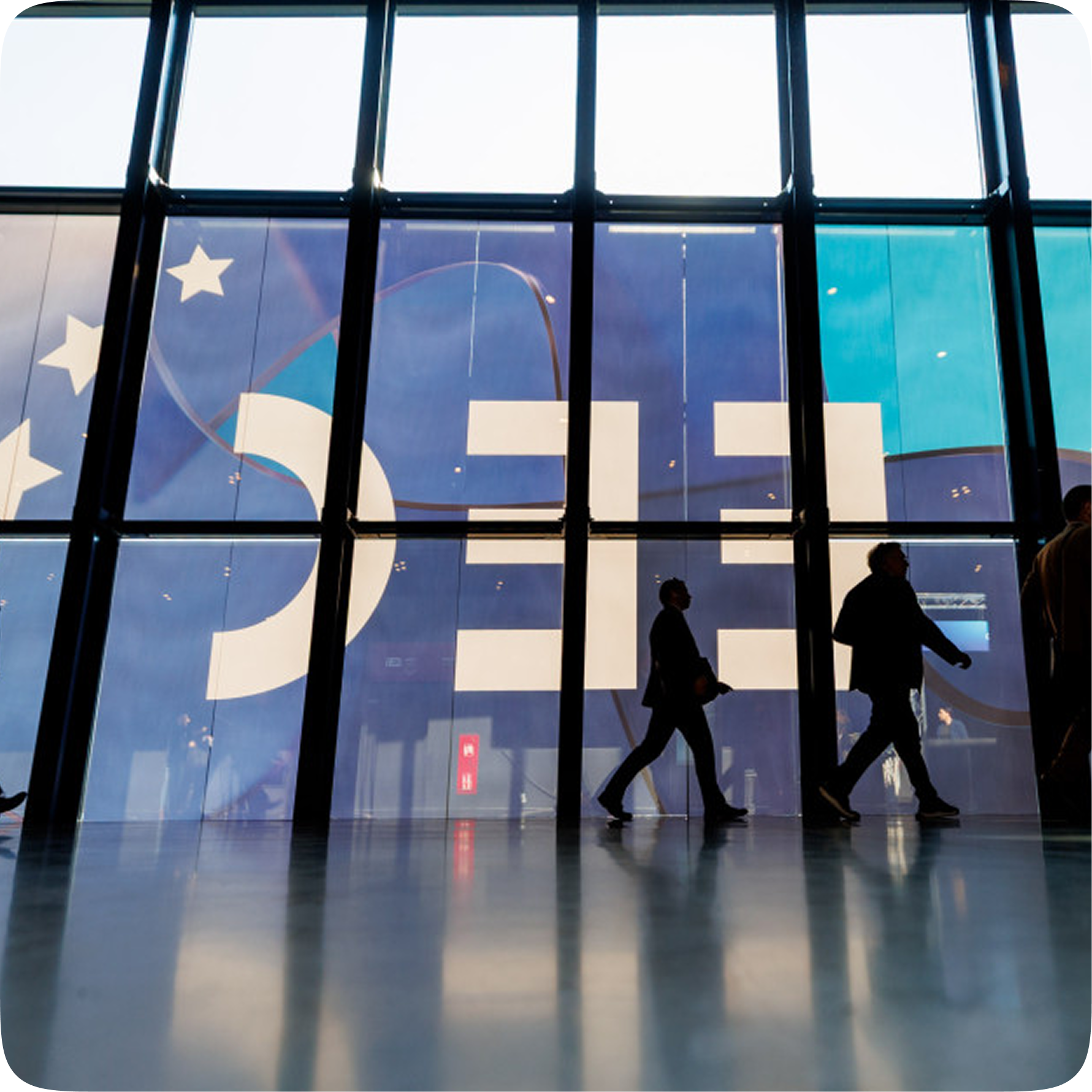sylwetki mężczyzn przechodzące przed banerem EEC