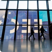 sylwetki mężczyzn przechodzące przed banerem EEC