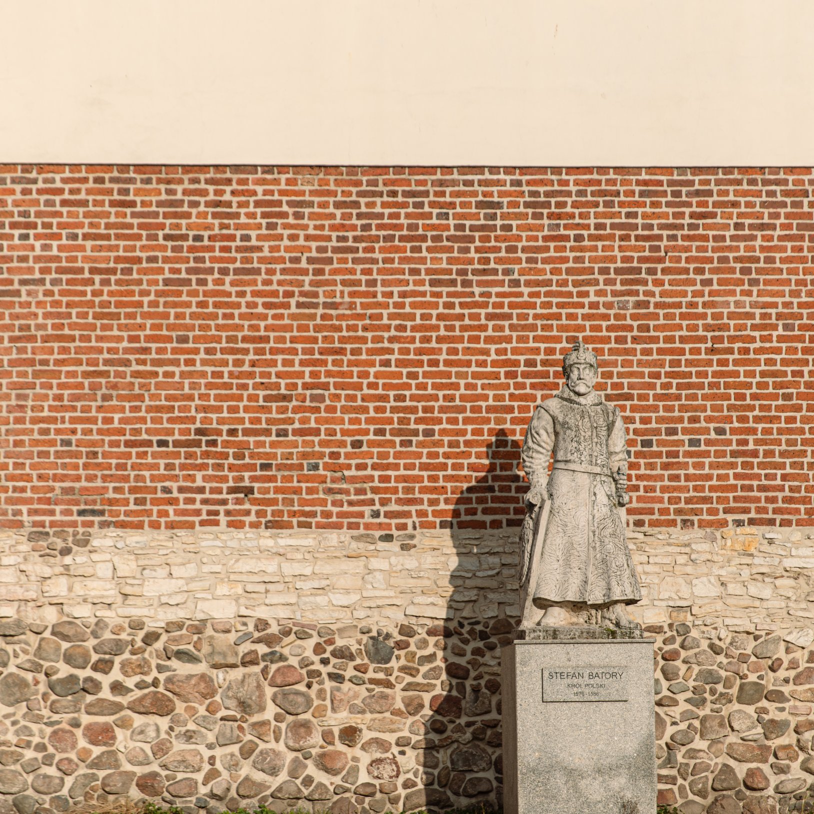 "Pomnik Stefana Batorego ustawiony na tle muru z cegły, kamienia i jasnego tynku. Rzeźba przedstawia monarchę w stroju historycznym, stojącego w dostojnej pozie, z mieczem u boku. Cokół z inskrypcją zawiera imię, tytuł i daty panowania króla."