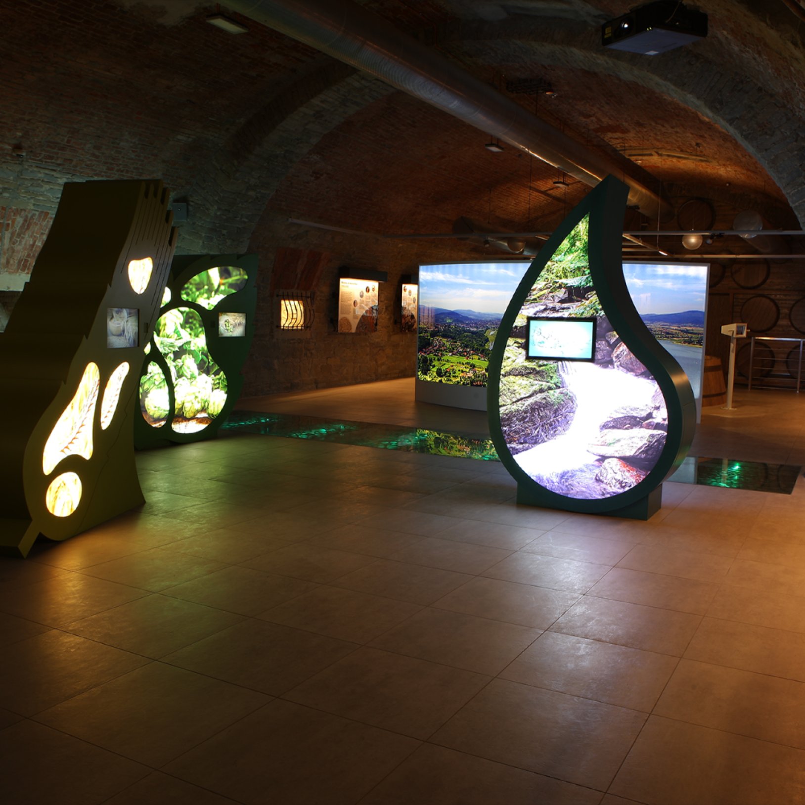 "Wnętrze Muzeum Browaru Żywiec z nowoczesnymi, podświetlanymi instalacjami multimedialnymi w kształcie kropli wody i ziaren słodu. Ekspozycja znajduje się w ceglanej, sklepionej sali z kamiennymi ścianami, tworząc połączenie nowoczesności z historycznym c