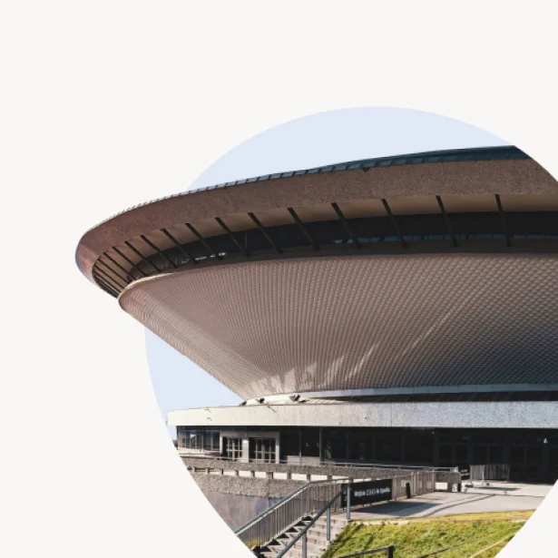 "Fragment charakterystycznego budynku Spodek w Katowicach, przedstawiony z dołu pod kątem. Widoczna jest dolna część dachu o talerzowatym, futurystycznym kształcie z siatkowaną fakturą.