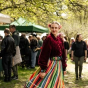 fotografia przedstawiająca kobietę w stroju ludowym na tle skansenu