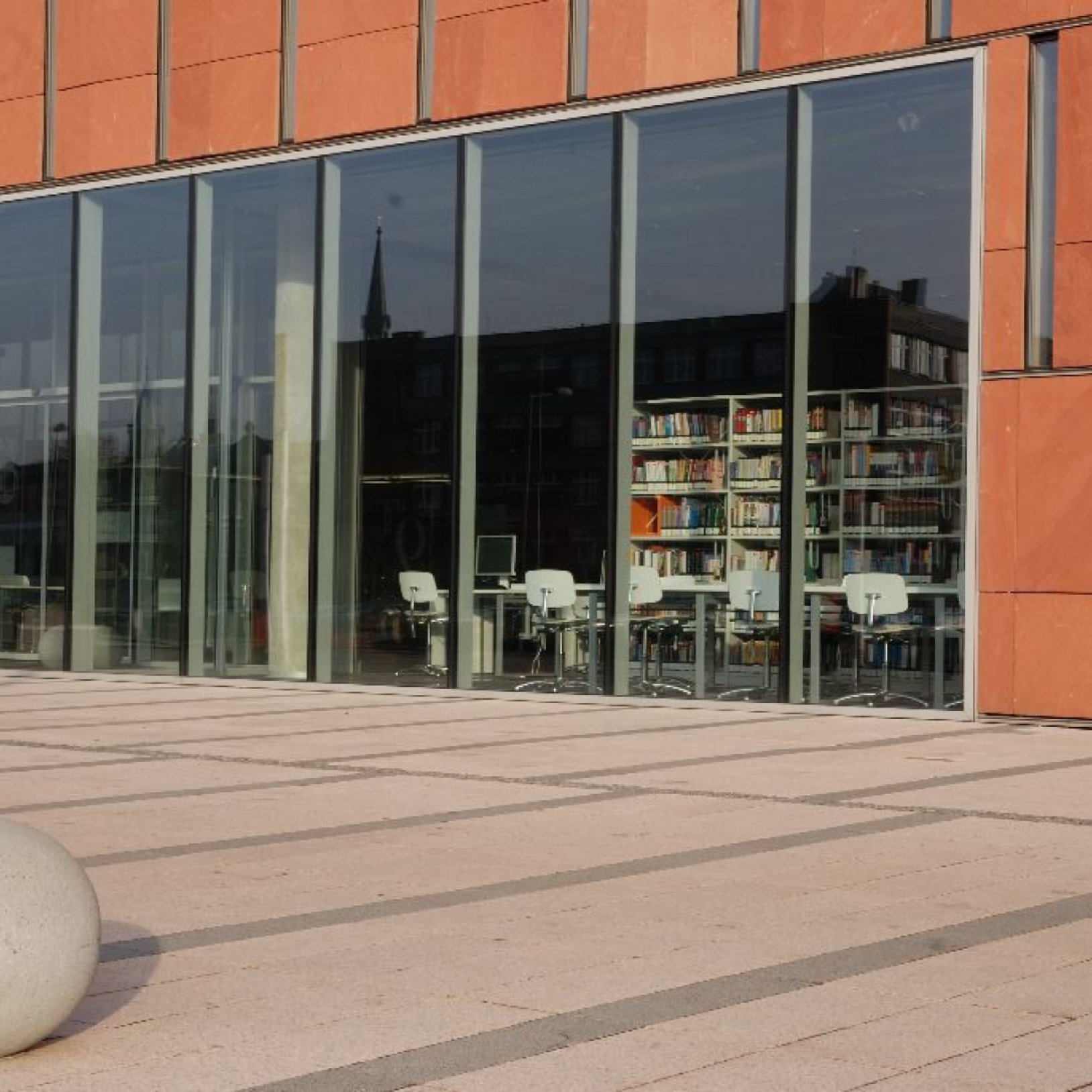 Wejście do galerii sztuki mieszczącej się w budynku z ciemnej cegły. Na drzwiach zawieszony baner wystawy Piotr Potworowski – malarstwo, z datami 4–29 czerwca. Wystawa promowana jest także plakatem widocznym w oknie po lewej stronie.