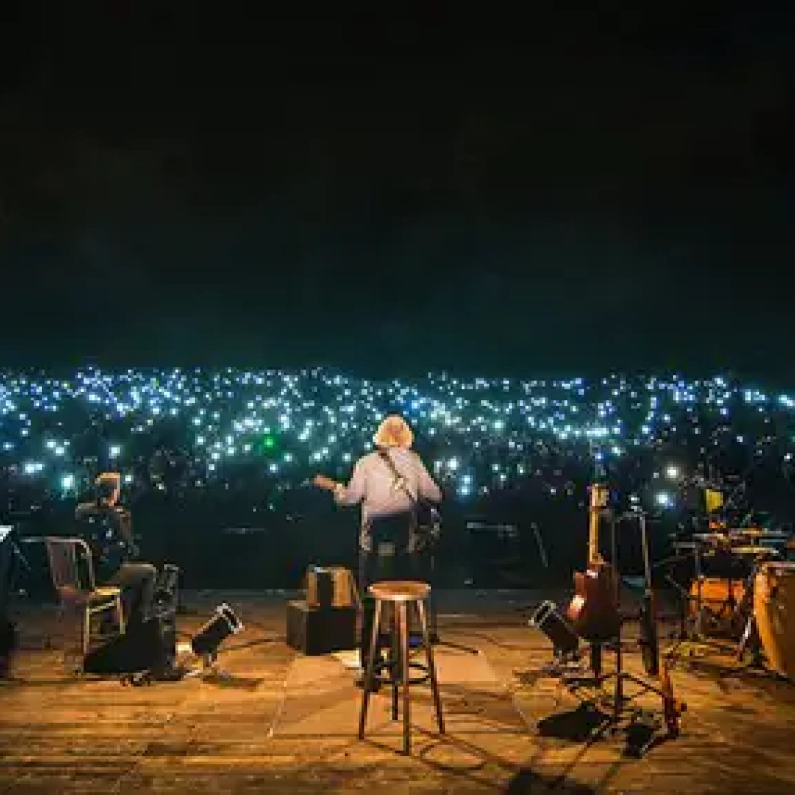 Gitarzysta na scenie podczas koncertu, przed publicznością z włączonymi światłami w telefonie